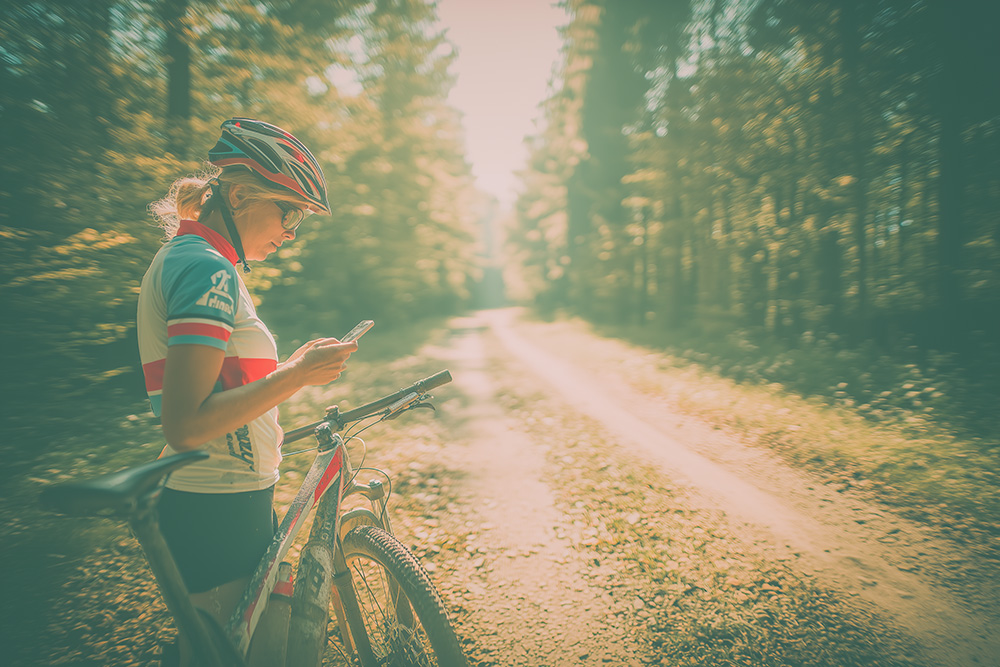Kvinna står vid sin cykel och tittar ner i sin smartphone